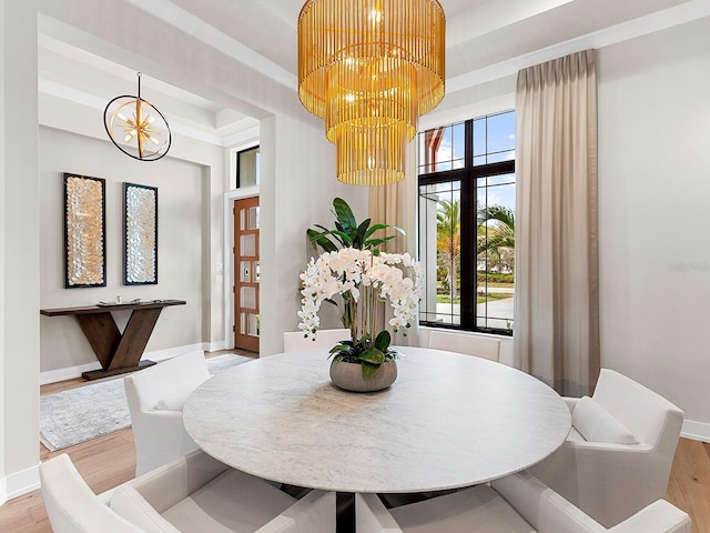 dining area with a notable chandelier, light hardwood / wood-style flooring, and a raised ceiling