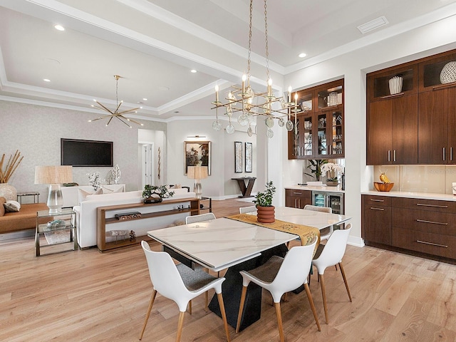 dining area featuring a chandelier, ornamental molding, bar, a tray ceiling, and light hardwood / wood-style flooring