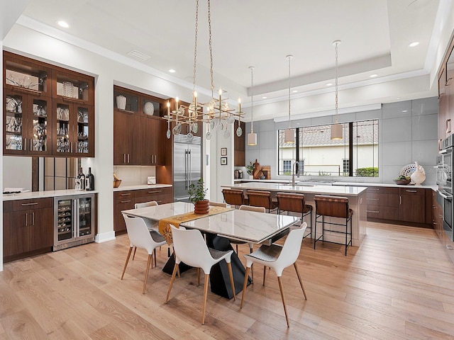 dining area featuring beverage cooler, a raised ceiling, sink, and light wood-type flooring