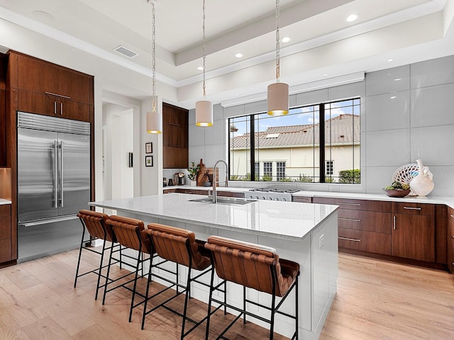 kitchen with a kitchen bar, sink, built in refrigerator, a center island with sink, and pendant lighting