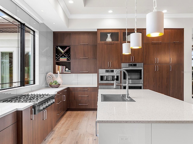 kitchen featuring appliances with stainless steel finishes, decorative light fixtures, sink, light stone countertops, and light wood-type flooring