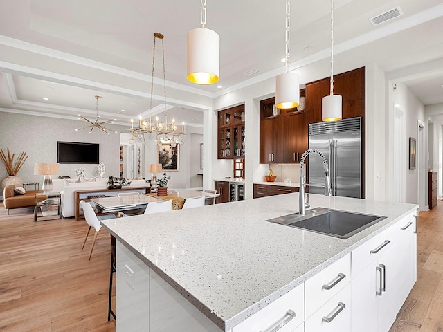 kitchen with white cabinets, an island with sink, hanging light fixtures, and built in fridge