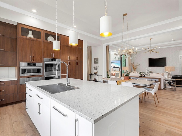 kitchen with pendant lighting, white cabinetry, an island with sink, sink, and light stone countertops