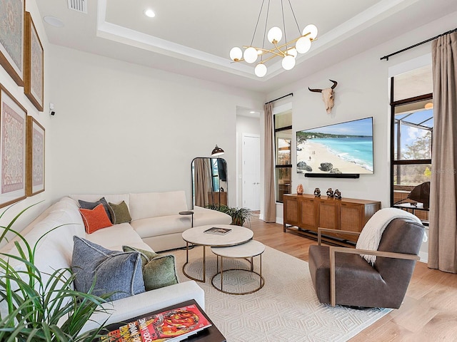 living room with light hardwood / wood-style floors, a raised ceiling, and a chandelier