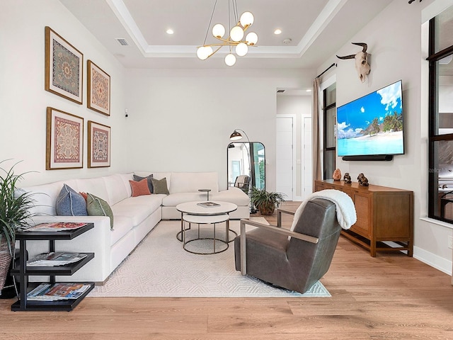 living room with a raised ceiling, a chandelier, and light hardwood / wood-style flooring