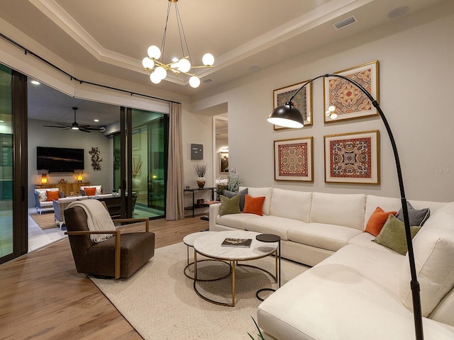 living room featuring hardwood / wood-style flooring, a raised ceiling, and ceiling fan with notable chandelier