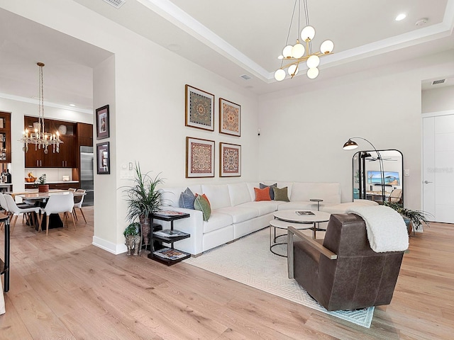 living room with a raised ceiling, a chandelier, and light hardwood / wood-style flooring