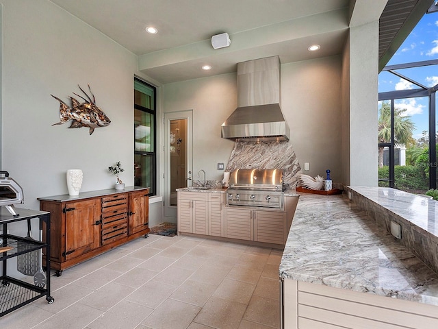 kitchen with sink, wall chimney range hood, light stone counters, and kitchen peninsula