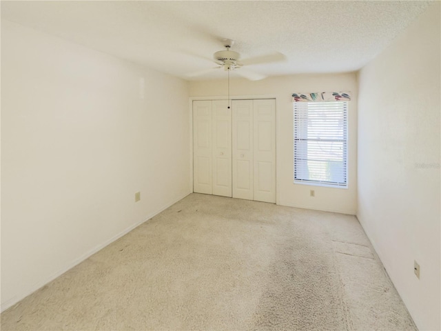 unfurnished bedroom featuring a textured ceiling, ceiling fan, a closet, and light colored carpet