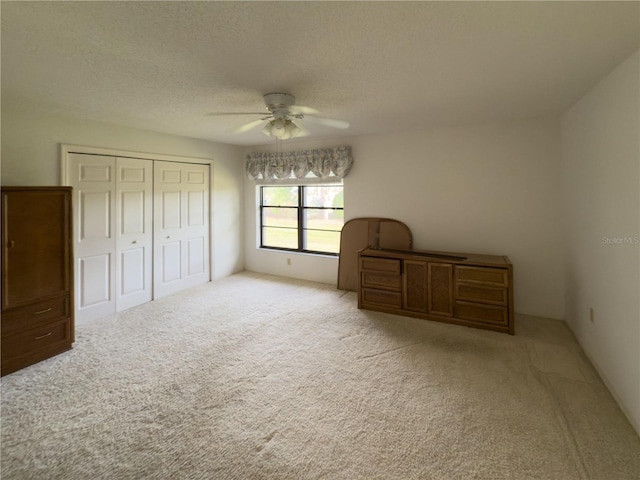 unfurnished bedroom featuring ceiling fan, a closet, light carpet, and a textured ceiling