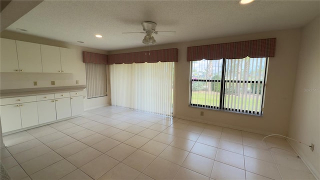 empty room featuring ceiling fan, light tile patterned floors, and a textured ceiling