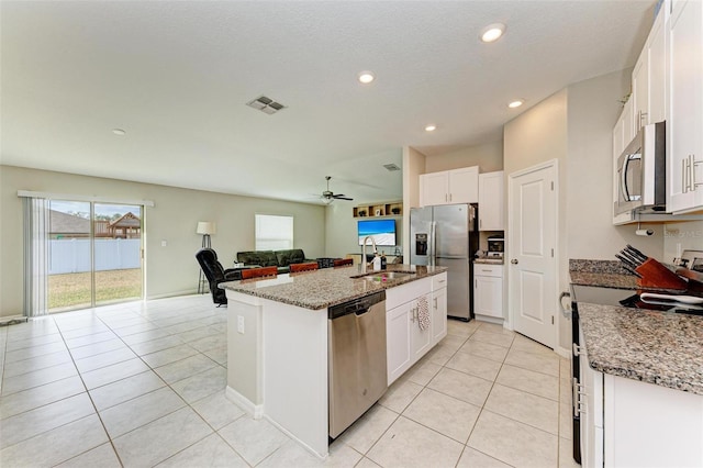 kitchen featuring white cabinets, light stone countertops, stainless steel appliances, and a center island with sink