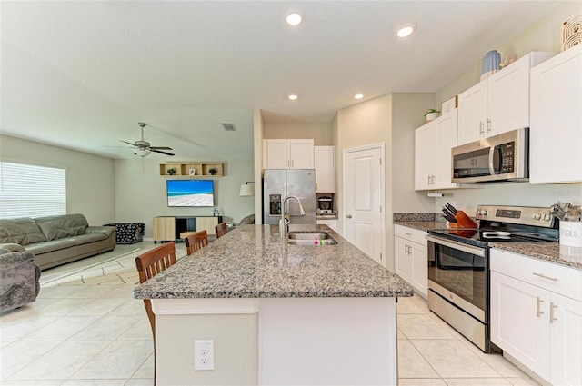 kitchen featuring white cabinetry, stainless steel appliances, a kitchen island with sink, dark stone counters, and sink