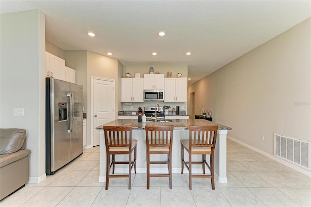 kitchen featuring white cabinetry, an island with sink, a breakfast bar area, stainless steel appliances, and dark stone counters