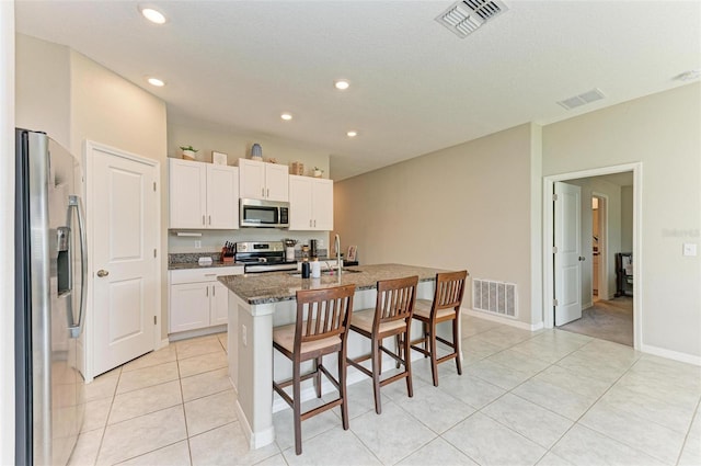 kitchen with white cabinetry, a center island with sink, a breakfast bar area, appliances with stainless steel finishes, and dark stone counters