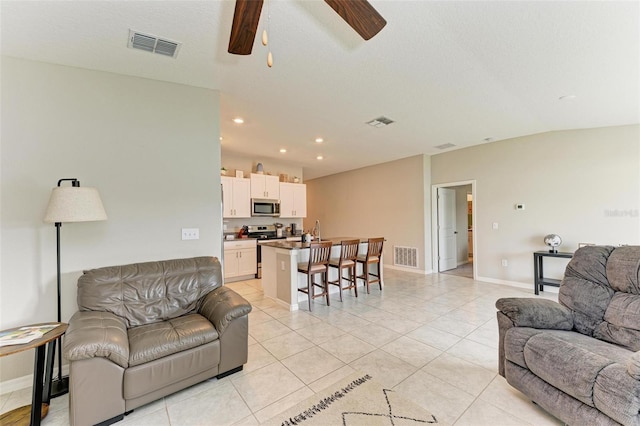 tiled living room featuring ceiling fan, vaulted ceiling, sink, and a textured ceiling