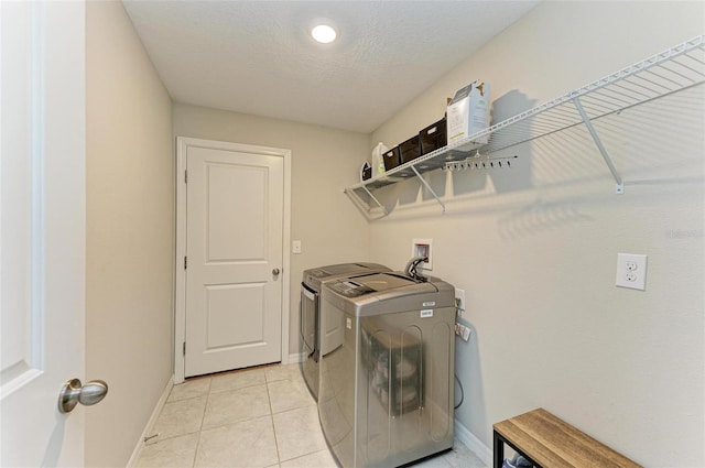 laundry area with a textured ceiling, light tile patterned floors, and washing machine and clothes dryer