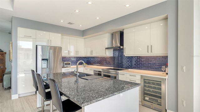 kitchen with dark stone counters, appliances with stainless steel finishes, wine cooler, and wall chimney range hood