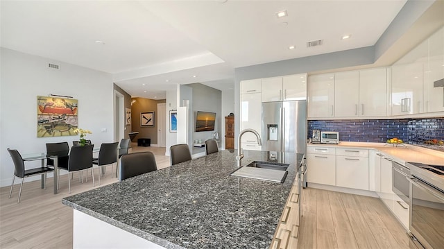 kitchen with an island with sink, light hardwood / wood-style floors, tasteful backsplash, white cabinetry, and sink