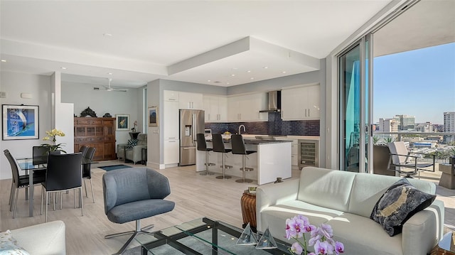 living room featuring floor to ceiling windows, light hardwood / wood-style floors, beverage cooler, ceiling fan, and sink