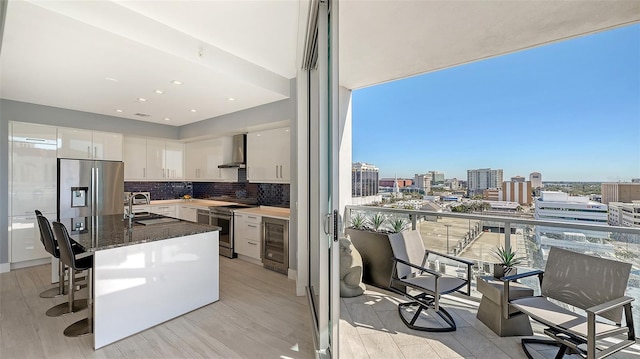 kitchen with stainless steel appliances, white cabinets, wall chimney exhaust hood, a breakfast bar, and wine cooler