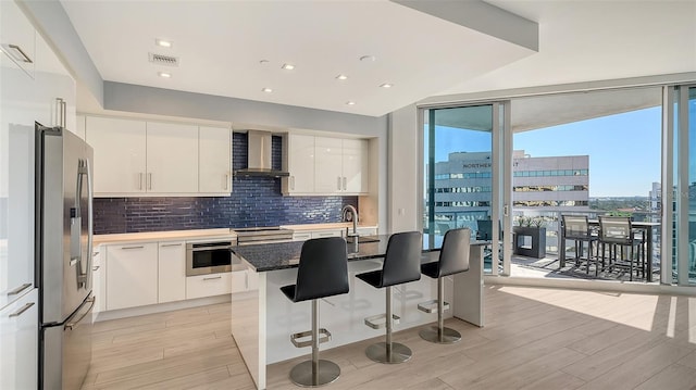 kitchen with stainless steel appliances, white cabinetry, wall chimney range hood, and a wall of windows