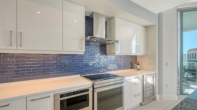 kitchen featuring stainless steel appliances, beverage cooler, wall chimney range hood, and white cabinetry