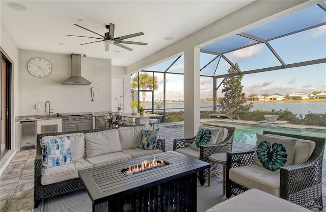 view of patio with sink, a lanai, a water view, an outdoor living space with a fire pit, and exterior kitchen