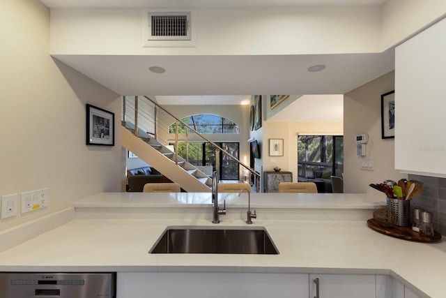 kitchen with stainless steel dishwasher, white cabinets, decorative backsplash, and sink