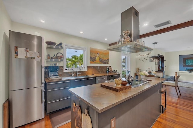 kitchen featuring decorative light fixtures, a center island, sink, appliances with stainless steel finishes, and island range hood