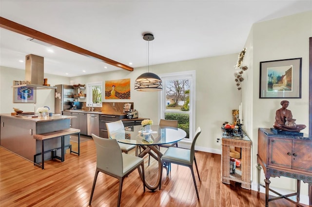 dining room featuring light wood-type flooring, beamed ceiling, and sink