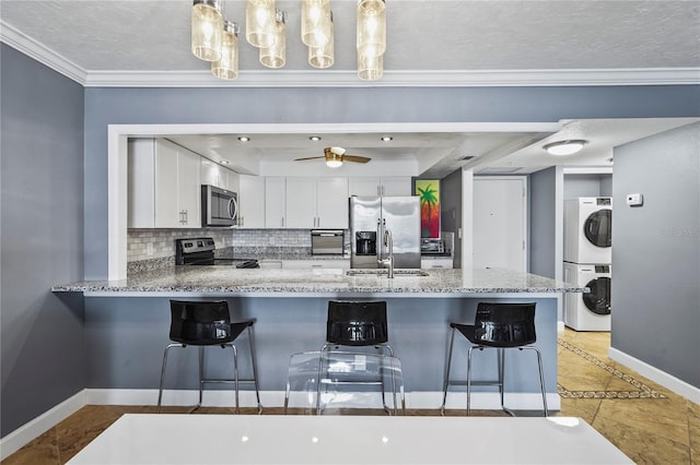 kitchen with white cabinets, appliances with stainless steel finishes, sink, hanging light fixtures, and stacked washer and clothes dryer