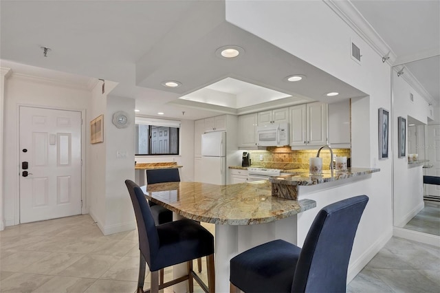 kitchen featuring white appliances, white cabinets, a kitchen bar, dark stone counters, and kitchen peninsula