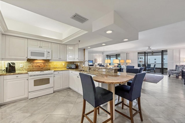 kitchen featuring white appliances, white cabinetry, sink, a raised ceiling, and kitchen peninsula