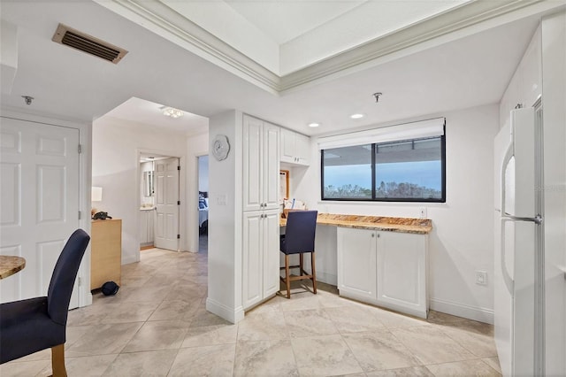 kitchen featuring white cabinetry, ornamental molding, and white fridge