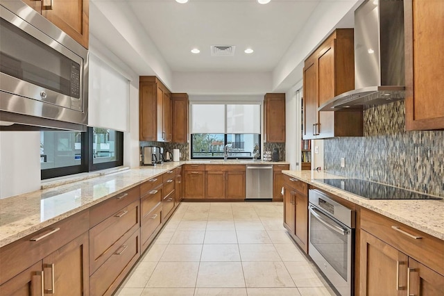 kitchen featuring appliances with stainless steel finishes, sink, light stone counters, and wall chimney range hood