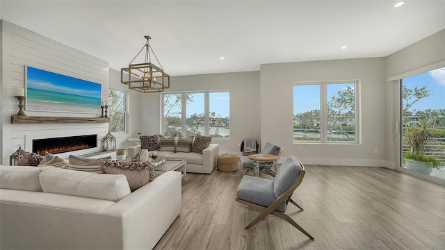 living room with light wood-type flooring, a healthy amount of sunlight, a fireplace, and a notable chandelier