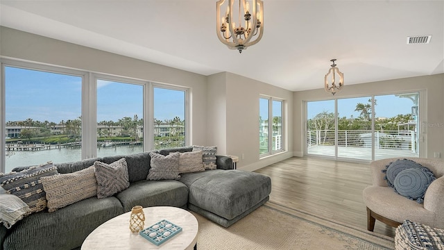 living room featuring light wood-type flooring, a chandelier, a water view, and plenty of natural light