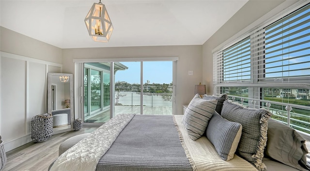 bedroom featuring light hardwood / wood-style floors, multiple windows, access to outside, and a water view