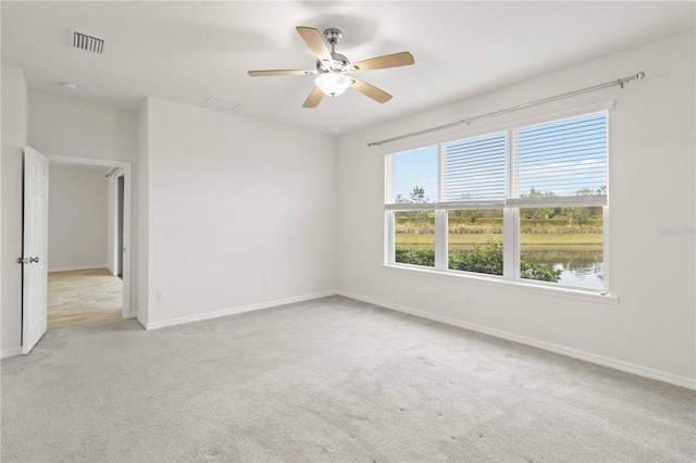 empty room featuring ceiling fan, light carpet, and a water view