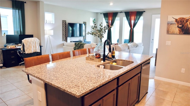 kitchen with dishwasher, a wealth of natural light, sink, light tile patterned flooring, and light stone counters