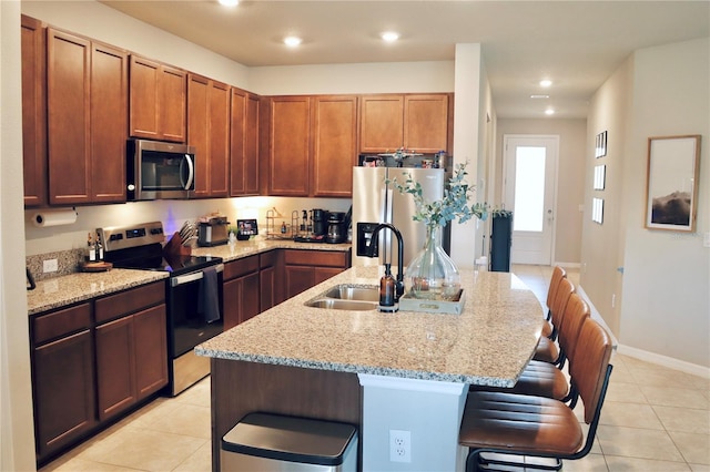 kitchen with sink, a kitchen island with sink, light stone countertops, appliances with stainless steel finishes, and a kitchen breakfast bar