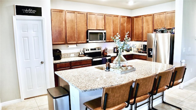 kitchen with a kitchen breakfast bar, appliances with stainless steel finishes, light stone counters, and a kitchen island with sink