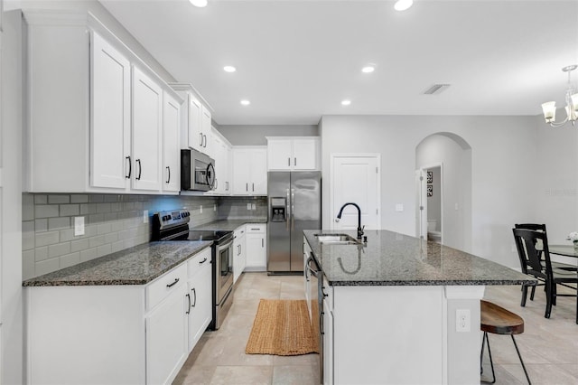 kitchen featuring white cabinetry, an island with sink, stainless steel appliances, dark stone counters, and sink