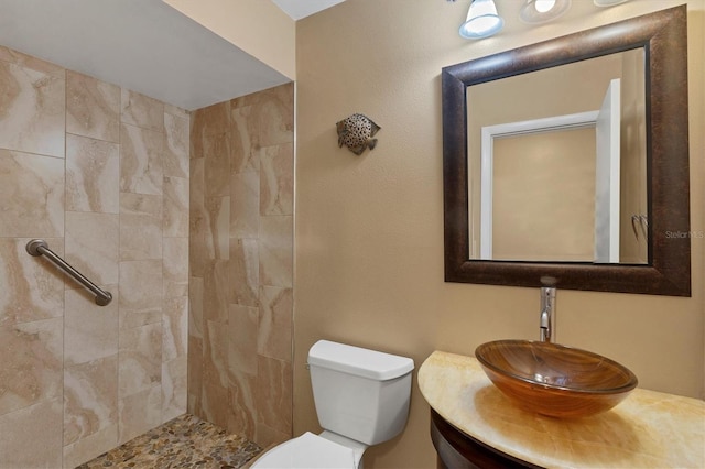 bathroom with toilet, a tile shower, and vanity