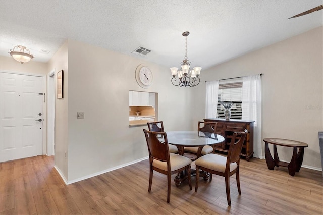 dining area with a textured ceiling, light wood-type flooring, an inviting chandelier, and vaulted ceiling