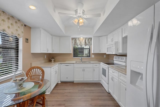 kitchen featuring white appliances, light wood-type flooring, a tray ceiling, sink, and white cabinetry