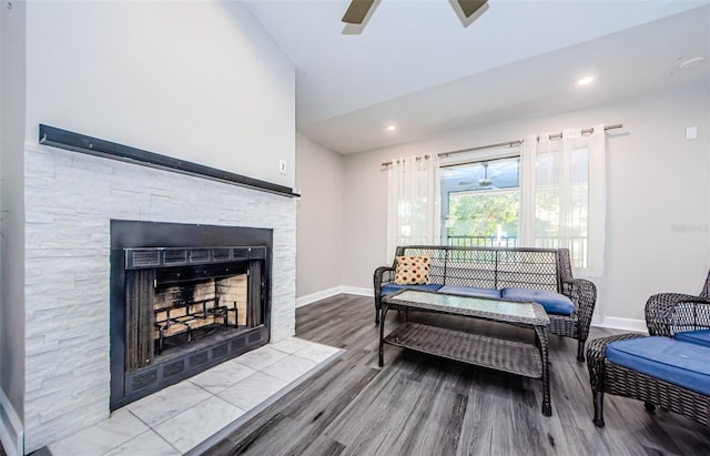 living room with wood-type flooring, a stone fireplace, and ceiling fan