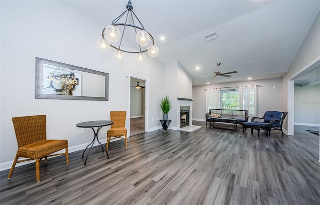 sitting room featuring ceiling fan with notable chandelier, hardwood / wood-style floors, a large fireplace, and high vaulted ceiling