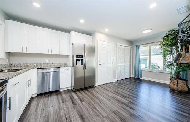 kitchen with dark hardwood / wood-style flooring, light stone countertops, white cabinetry, and appliances with stainless steel finishes